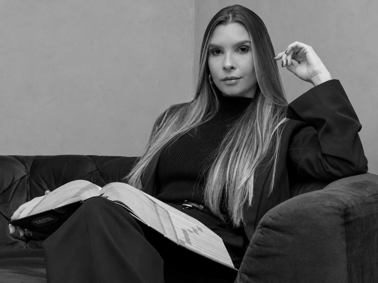 Retrato em preto e branco de mulher sentada no sofá, com um livro aberto no colo.