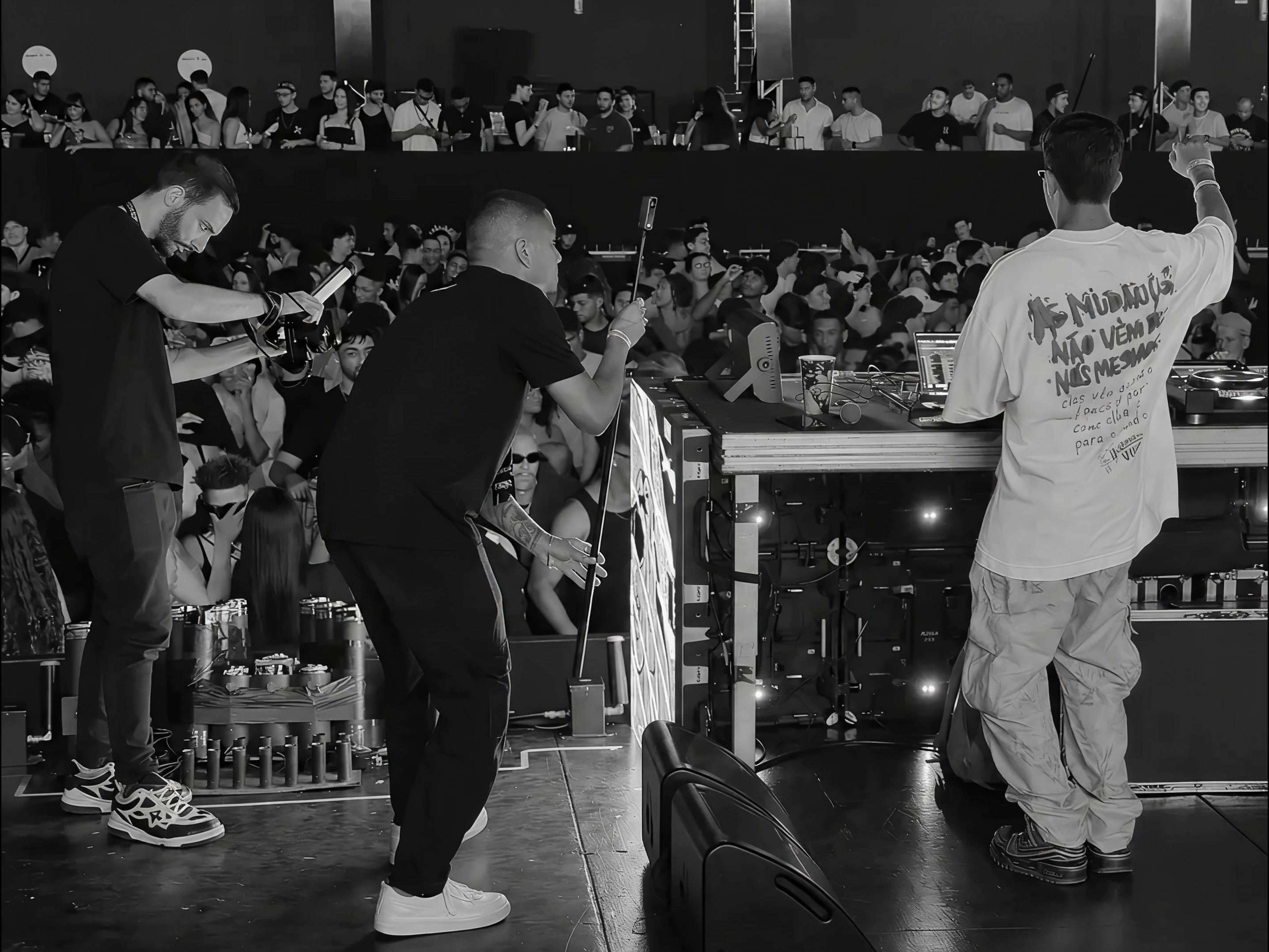 Bastidores de uma captação audiovisual em evento, com operadores de câmera, DJ e público.